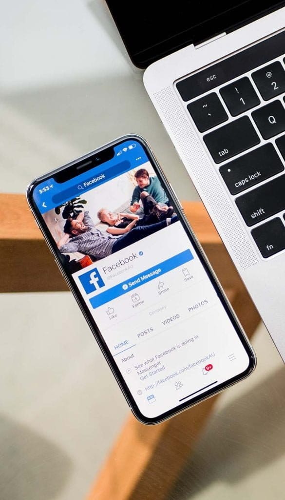 Mobile phone on a 45-degree tilt, with Facebook page displayed. Phone is next to white computer keyboard with only a few of the left side keys showing in the image.